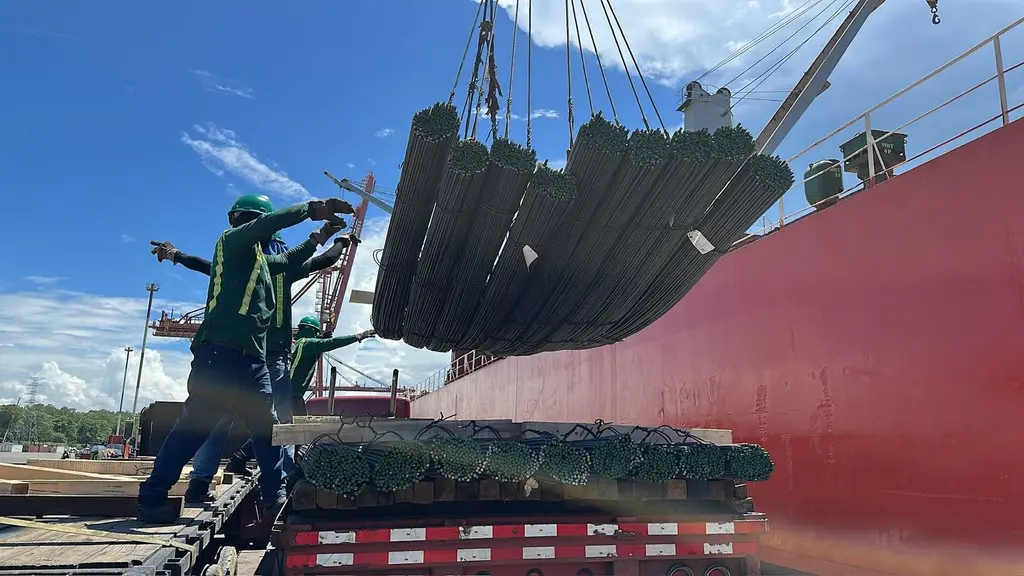 Crew guiding rebar bundles onto a truck beside a red hull