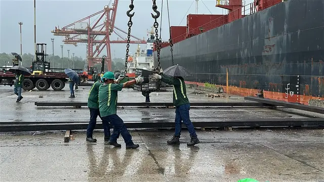 Crew guiding a steel plate alongside the vessel in the rain