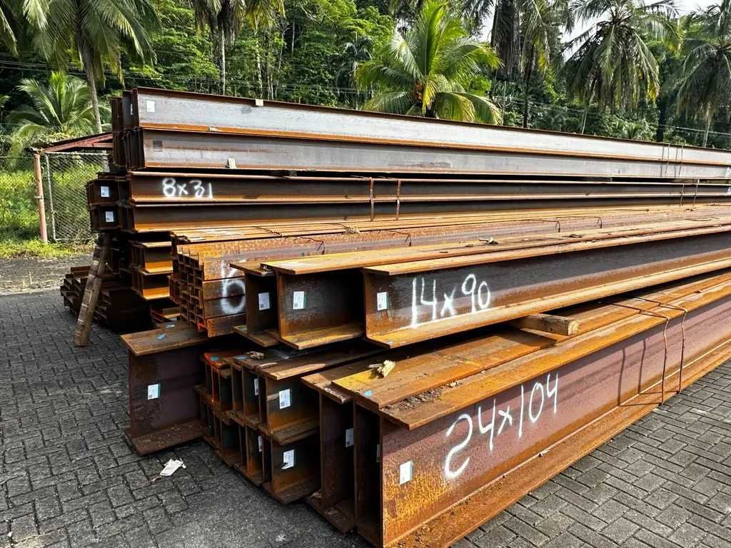 Stacked steel beams with their sizes painted on, palm trees behind