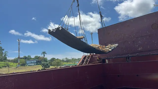 Steel plates lifted over the ship's side, palm trees on shore